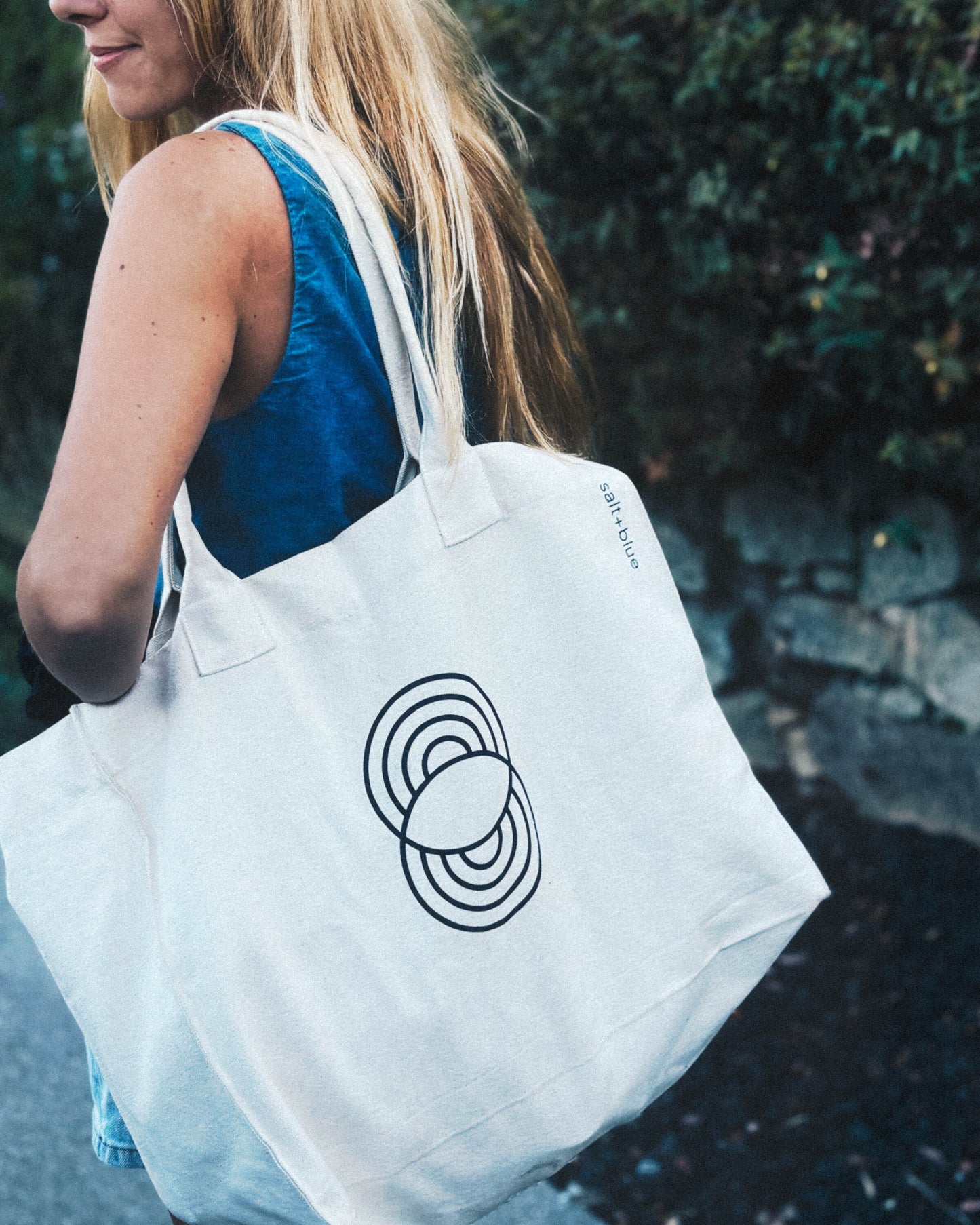 Woman carrying the Carryall Tote - Seashell (Natural) a 100% organic cotton, natural all-side gusset tote bag with blue salt+blue logo.