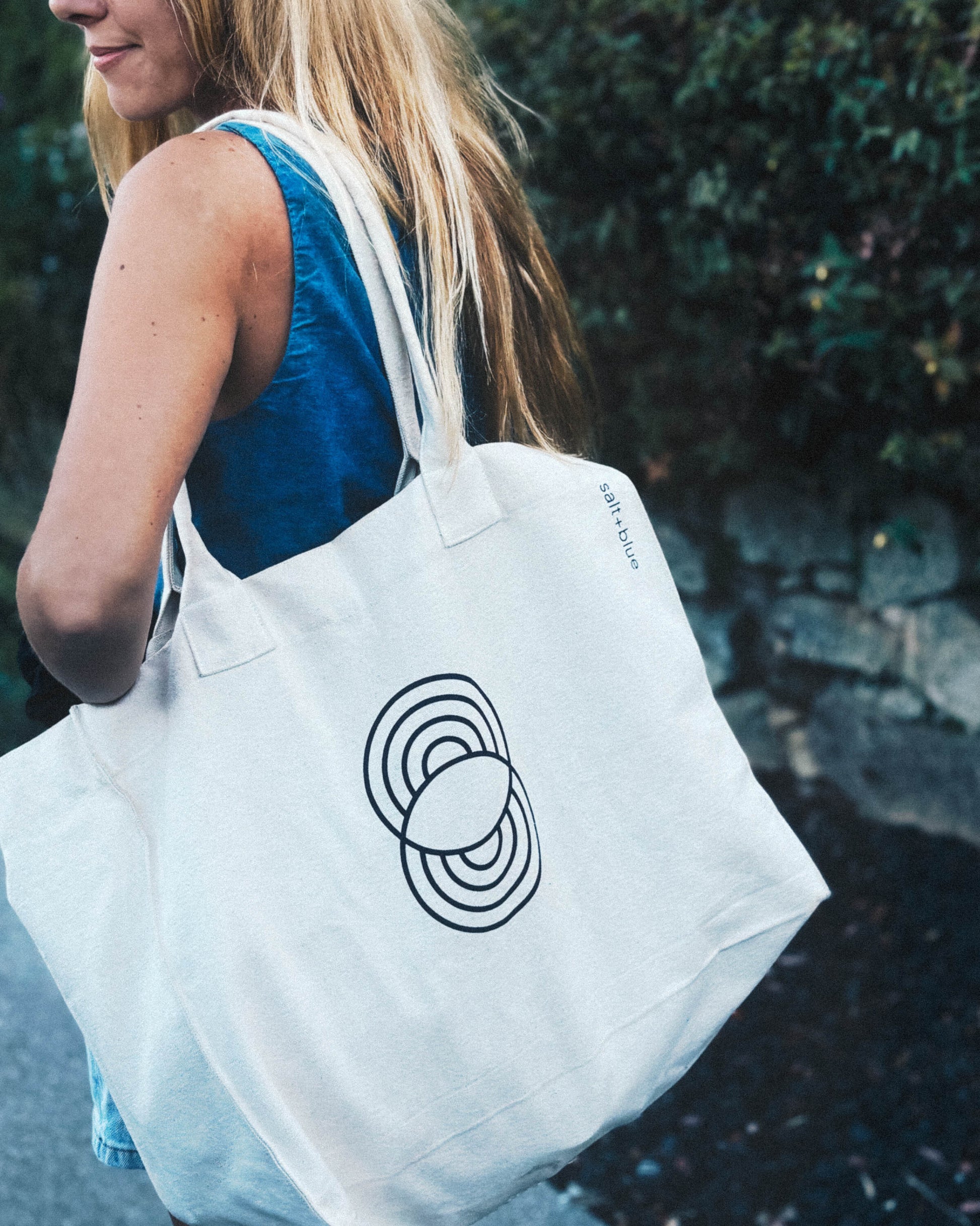 Woman carrying the Carryall Tote - Seashell (Natural) a 100% organic cotton, natural all-side gusset tote bag with blue salt+blue logo.