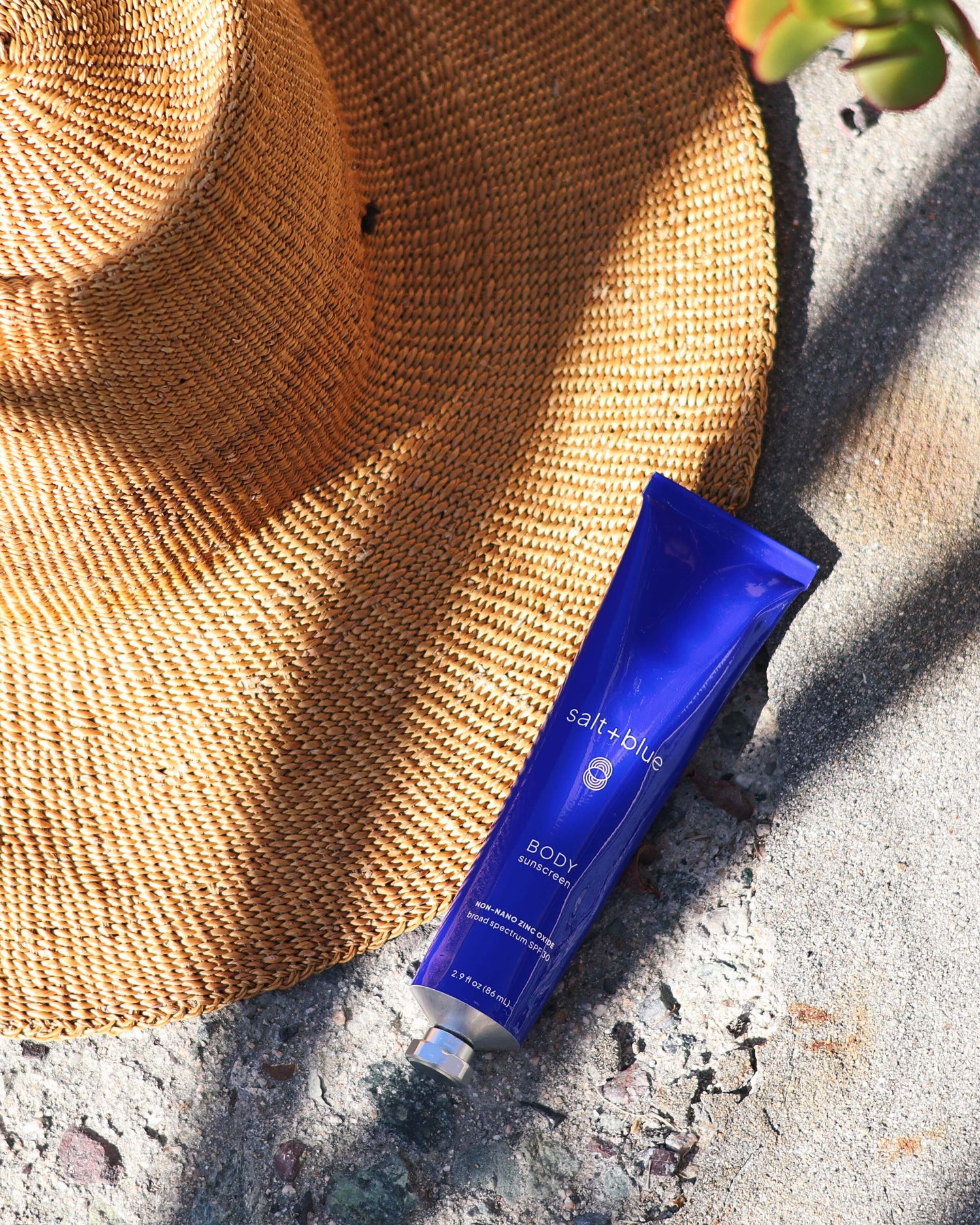 Blue tube of salt+blue sunscreen on a stone surface with a straw hat in the background