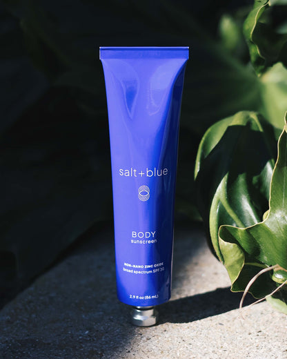 Blue tube of salt+blue sunscreen on a dark background with green leaves