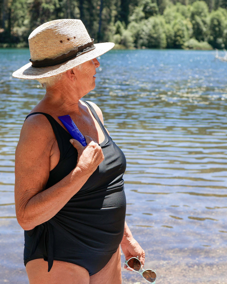 Woman wearing hat holding salt+blue BODY sunscreen tube