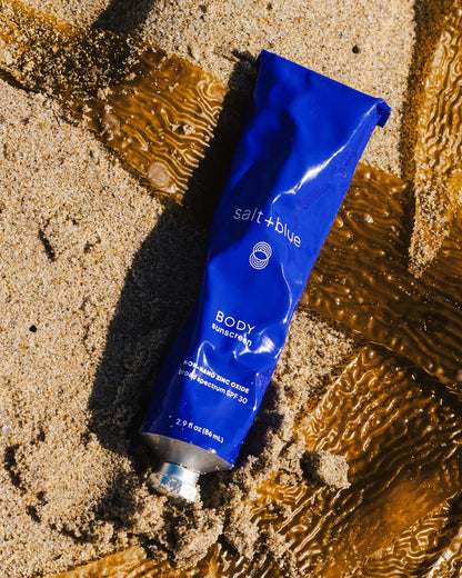 Blue tube of salt+blue body sunscreen on wet sand