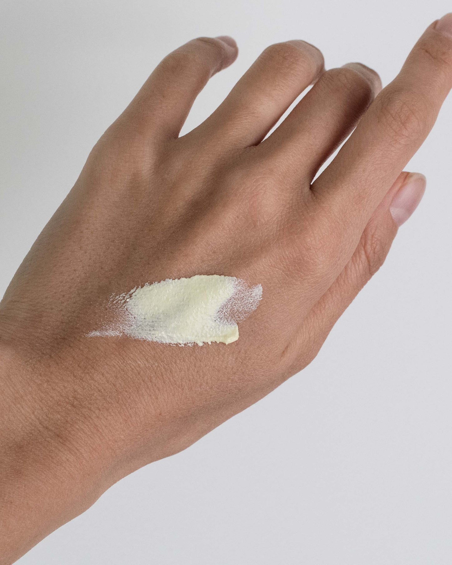 Hand with a small amount of sunscreen on a plain background
