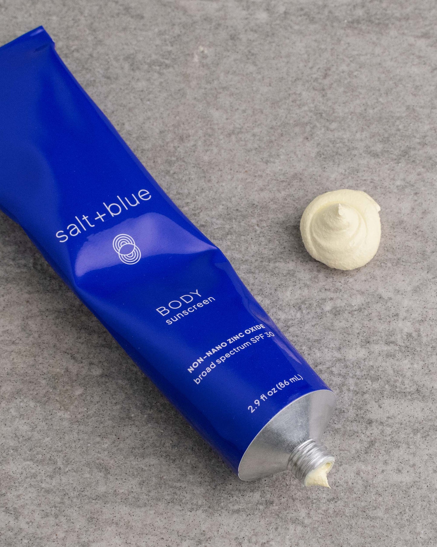 BODY sunscreen tube with a sample of sunscreen on a gray stone surface